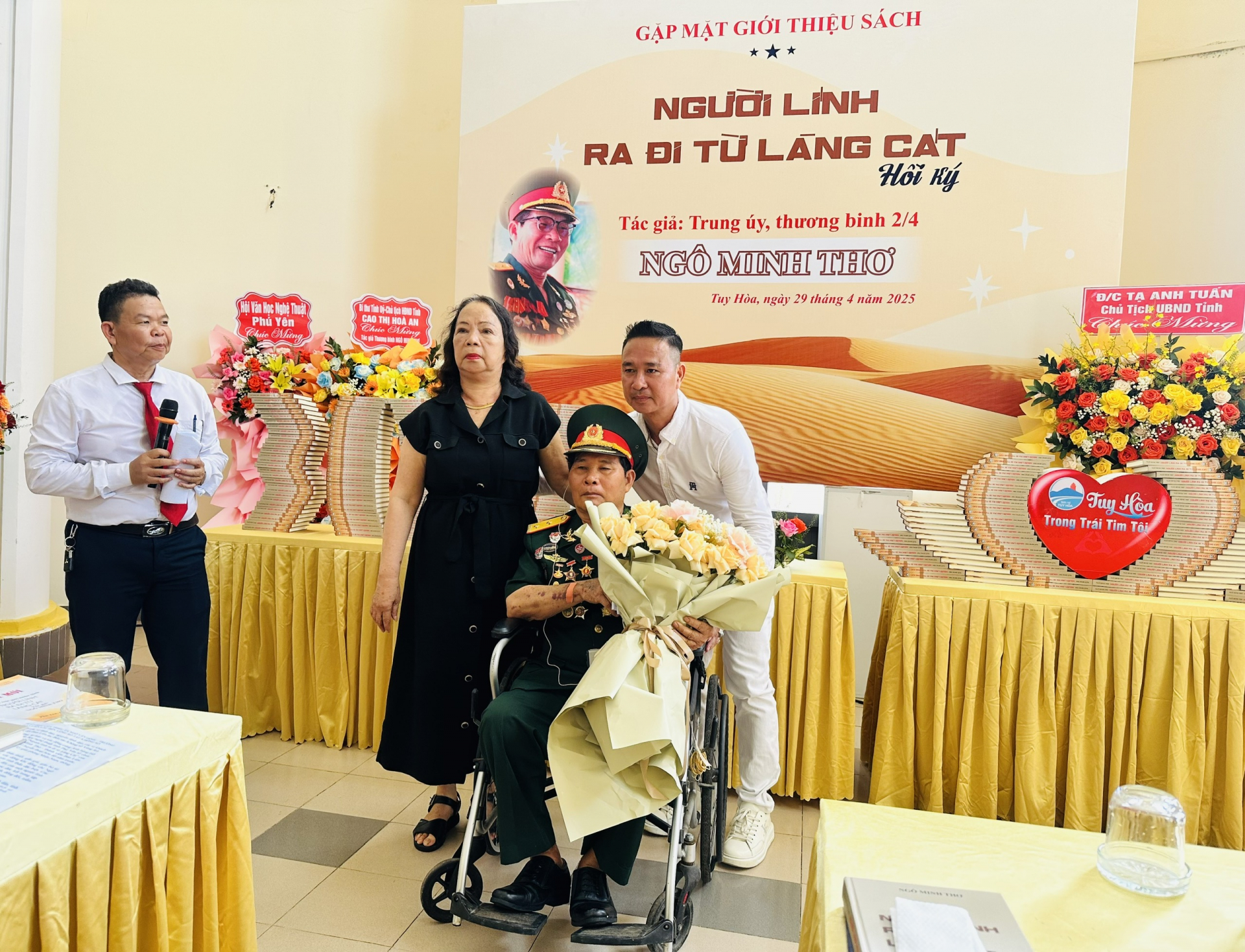 Trung úy - thương binh Ngô Minh Thơ cùng vợ - bà Nguyễn Thị Hoa và con trai cả Ngô Minh Thông nhận hoa chúc mừng trong buổi gặp mặt giới thiệu sách. Ảnh: YÊN LAN