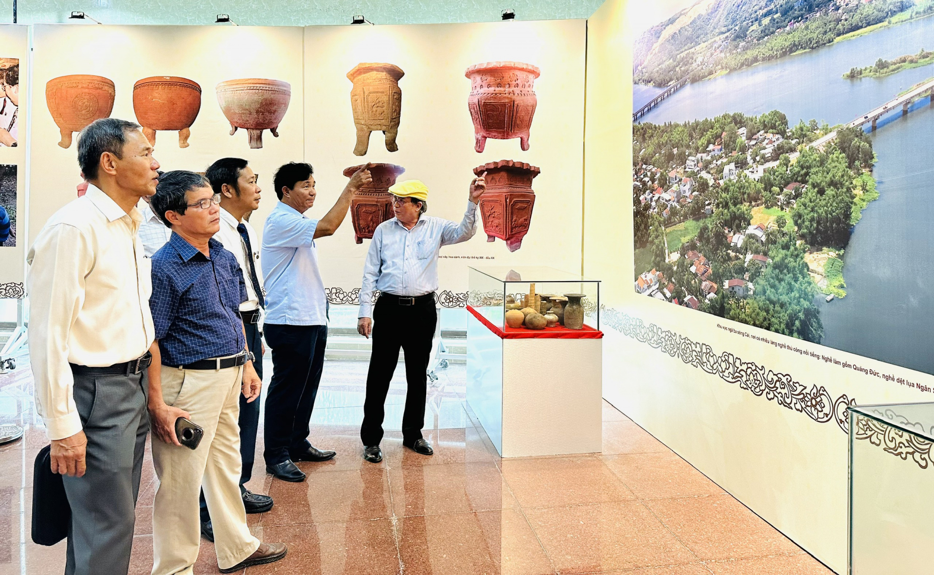 Former PPC Vice Chairman Phan Dinh Phung (far right), discussing with delegates in front of a photograph of the confluence of the Cái River - an area known for its many renowned traditional craft villages, including Quang Duc pottery, silk weaving in Ngan Son, and bamboo basket boat making in Phu My